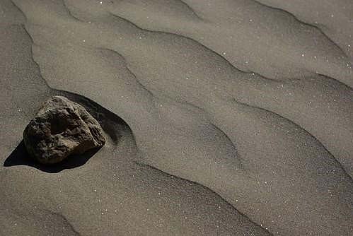 A craggy-textured rock is on the rippled sandy shore of a beach. 