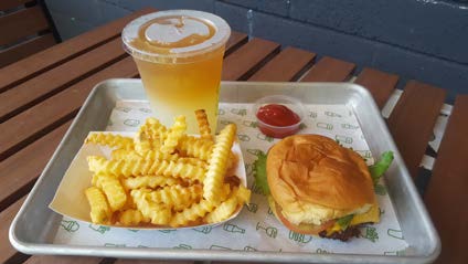 a tray with a hamburger, fries, cup of ketchup, and a yellow drink