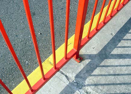 barred orange fence near the road is casting a shadow on the sidewalk