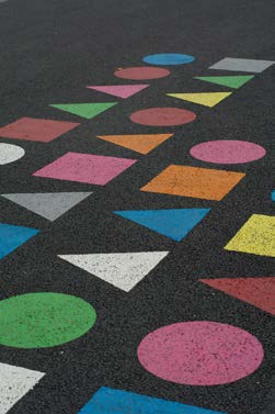 A pattern of circles, squares, and triangles in bright colors contrasted on an asphalt surface. 